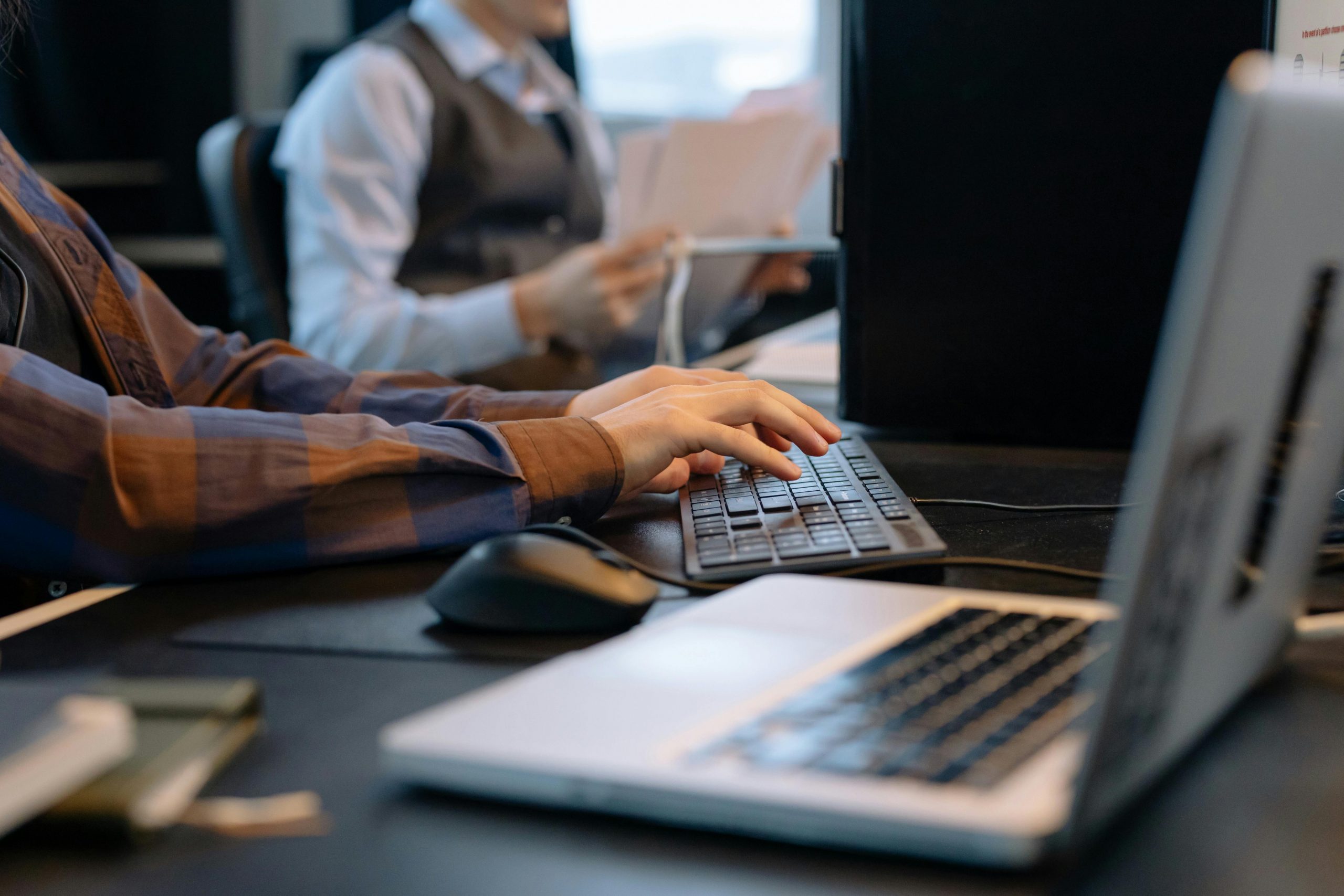 two people working at desks, typing on desktop keyboards