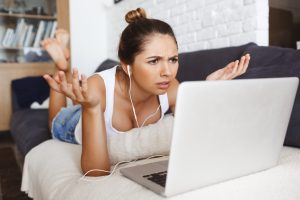 woman wearing earphones plugged into a laptop, frowning