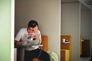 frustrated man sitting in a booth using a sticker-covered laptop